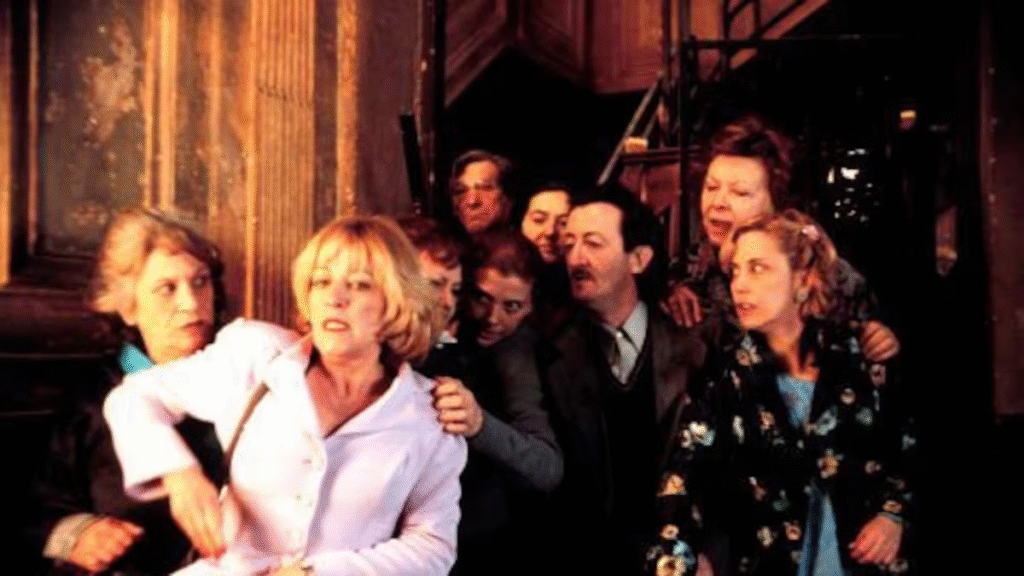 Fotograma de la película "La Comunidad" de Álex de la Iglesia. Carmen Maura, en primer plano, y todos los vecinos amontonados tras de ellas en el rellano del edificio.